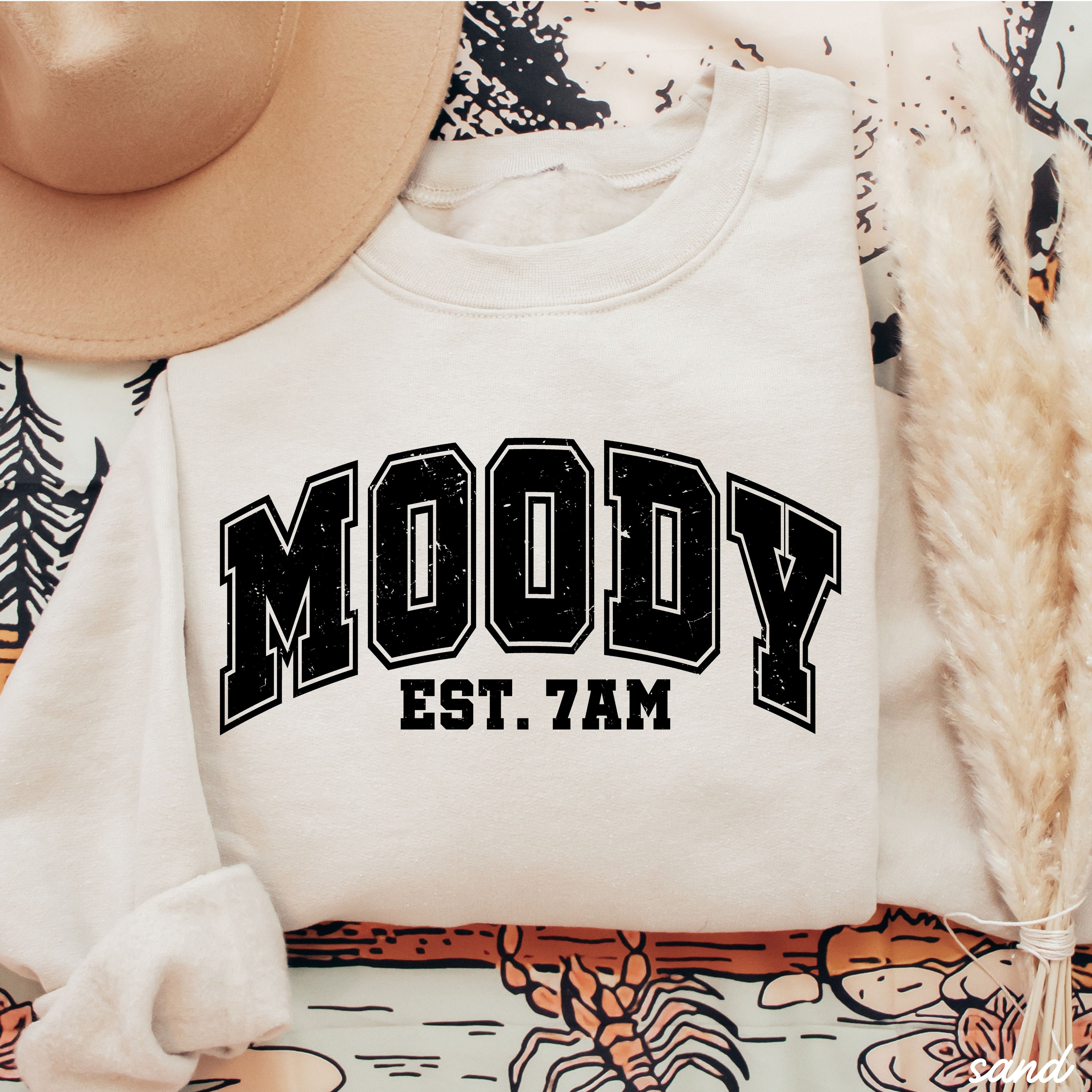 Moody 7am Sweatshirt 7 Colors S-3X displayed on a patterned background with hat and decor.
